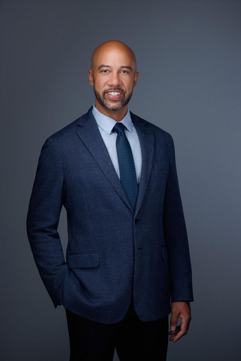professional portrait of Kenneth Thrower, founder of Fidelis CPAs. Kenneth wears a blue suit, collared shirt, and tie, and smiles at the camera